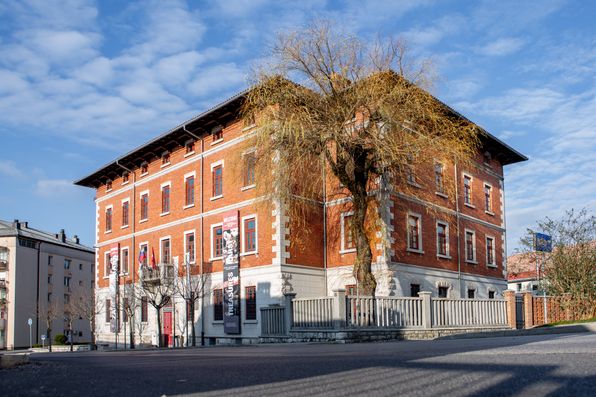 Notranjski muzej Postojna z moderno muzejsko stavbo in urejenim pročeljem v ospredju.