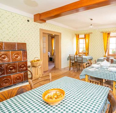 Tradicionalna jedilnica v Notranjski hiši s krušno pečjo, lesenimi tramovi in pogrnjenimi mizami.