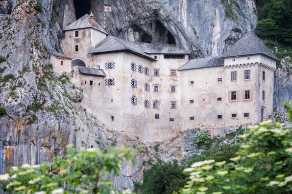 Predjamski grad vgrajen v visoko skalno steno nad zeleno dolino.